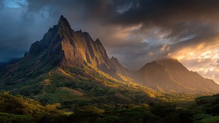 Majestic jagged mountains emerge from lush green foliage under a dramatic stormy sky at sunset