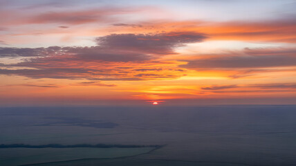 Illustration of a dramatic sunset over a vast landscape with vibrant sky and golden clouds at the horizon