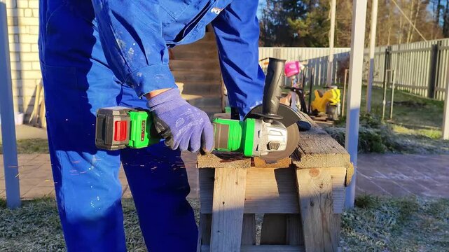 A worker cuts metal with a cordless angle grinder creating sparks. Close-up of a power tool in action at a construction site. Vertical video of manual labor and DIY projects