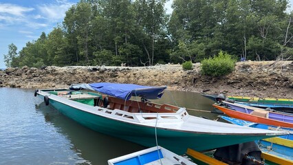 Colorful boats are anchored at the mouth of a calm river with lush green trees. © faqih