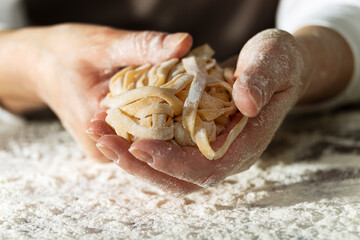 Caucasian female hands holding raw fettuccine noodles after drying