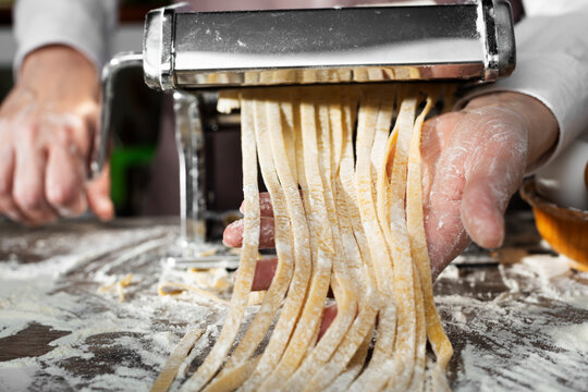 Caucasian female hands making fettuccine noodles using mechanical pasta machine - Powered by Adobe