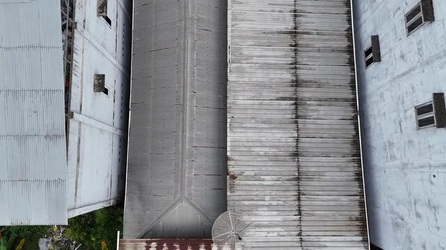 A drone shot showing the view from above a grey metal roof flanked by industrial concrete buildings.