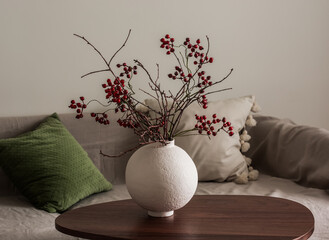 Dried cranberry branches in a ceramic vase on a wooden table near the sofa in the living room