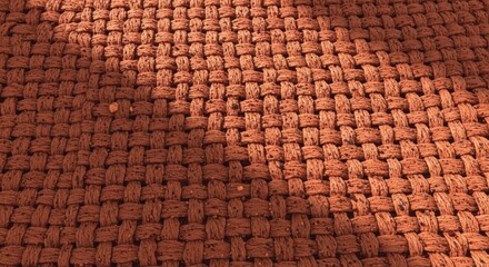 Closeup of a woven brown rug with a textured surface and a diagonal shadow casting a warm, inviting ambiance on the floor covering