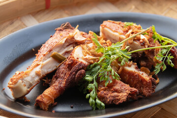 Crispy fried chicken drumstick with herbs and fried garlic on black plate, savory comfort food served hot