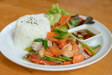 Shrimp stir fry with vegetables and steamed rice served with salad and dipping sauce on wooden table, appetizing home meal