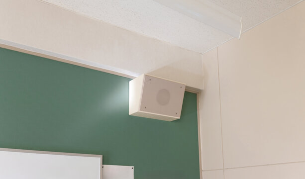 A white speaker installed in the corner near the ceiling of a school classroom