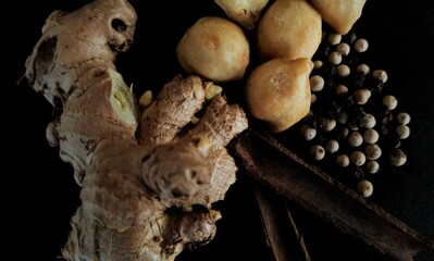 spices consisting of ginger, candlenut, pepper, and cinnamon on a black background.