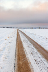 Long straight dirt road over snowy field towards the horizon