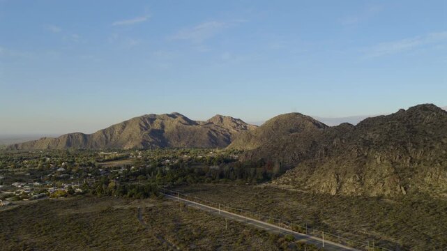 Chilecito valley and rugged hills under blue sky, sunlit slopes and scattered houses in picturesque Argentinian landscape.