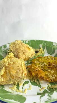 Indonesian fried snacks featuring bakwan and stuffed tofu on a green-white enamel plate. Traditional oily unhealthy street food. closeup. copy space