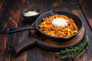 Classic pasta bolognese with savory meat ragu and parmesan shreds served in rustic skillet on vintage wooden surface with herbs.