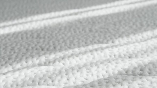 Soft white mattress texture with morning sunlight. Quilted fabric pattern and cozy bedroom atmosphere.