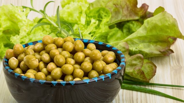 Bowl of fresh green peas with lettuce and chives on a wooden surface - Powered by Adobe