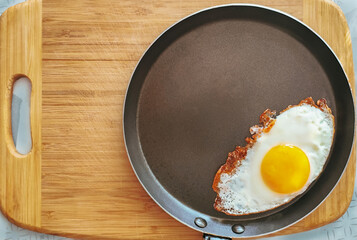 Stainless steel frying pan with a fried egg on a wooden table.