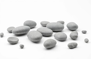 Photo featuring several grey stones scattered against a plain white backdrop. The rounded stones display natural textures. The composition creates a sense of minimalism and tranquility.