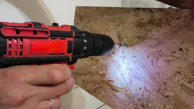 A man using Power drills drives a screw into an OSB board close-up. Assembling furniture, wall boards, repairs in the apartment