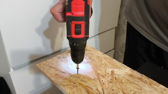 A man using Power drills drives a screw into an OSB board close-up. Assembling furniture, wall boards, repairs in the apartment