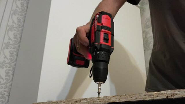 A man holds Power drills in his hand and screws into a wooden OSB board. Repair, assembly of furniture, construction. view from below