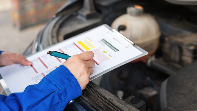 Action of a car service technician is checking on vehicle inspection checklist form during perform the maintenance job. Close-up and selective focus.