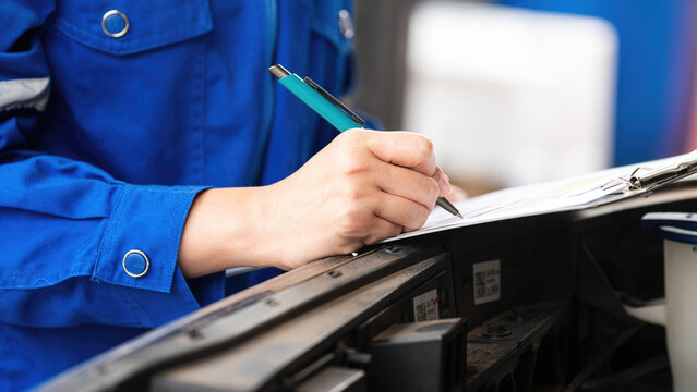 Action of a car service technician is checking on vehicle inspection checklist form during perform the maintenance job. Close-up and selective focus.