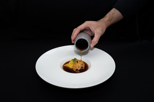 A Chef elegantly pouring sauce over a delicious dish, set against a dark background, evoking a sense of culinary artistry