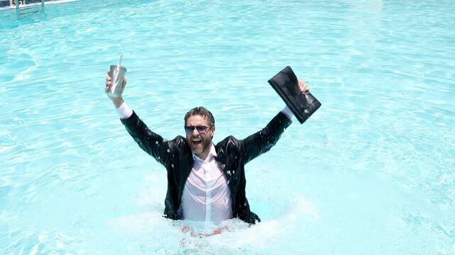 Funny businessman in suit working with computer on the sea beach. Summer holiday, outdoor and business travel concept. Crazy office worker. Man working on laptop computer sitting in cloth at poolside.