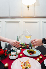 Festive cheers with fine dining. Two hands are holding wineglasses up to clink over a holiday table, there's gourmet meals