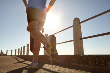 Man, legs and running with sunshine on promenade for workout, cardio exercise or outdoor training. Active, male person or runner with shoes or sneakers for physical activity, health or wellness