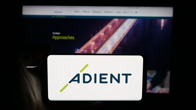 Stuttgart, Germany - 11-08-2025: Person holding cellphone with logo of automotive seating company Adient plc on screen in front of webpage. Focus on phone display.