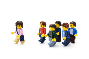 Naklejka premium Many lego minifigures in group are walking behind a girl or woman isolated on white. Editorial illustrative image of popular children plastic constructor.