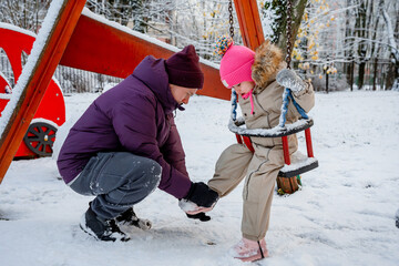 A father with his daughter, a three-year-old girl, on a swing on a snowy playground in winter