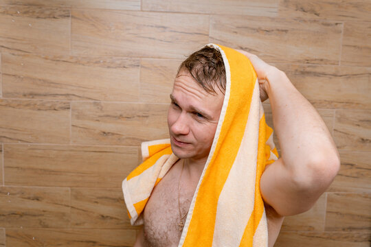 A young man wipes wet hair on his head with a towel after a shower