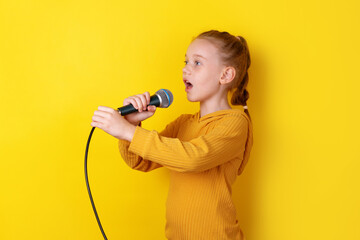 Cheerful young girl in yellow singing into a microphone against vibrant yellow background, expressing creativity and joy.
