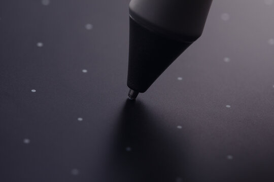 Close-up of a digital stylus tip touching a black graphic tablet surface with dotted grid, illustrating precision and technology.