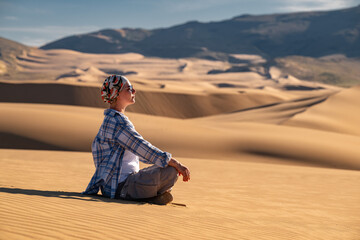 Serene woman hiker sits at sand dune and enjoys desert view at sunset. Mongol Els desert, Mongolia