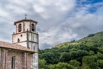 Fototapeta premium Historic Stone Church Bell Tower with Green Mountain Valley Landscape Background, Baztan Valley