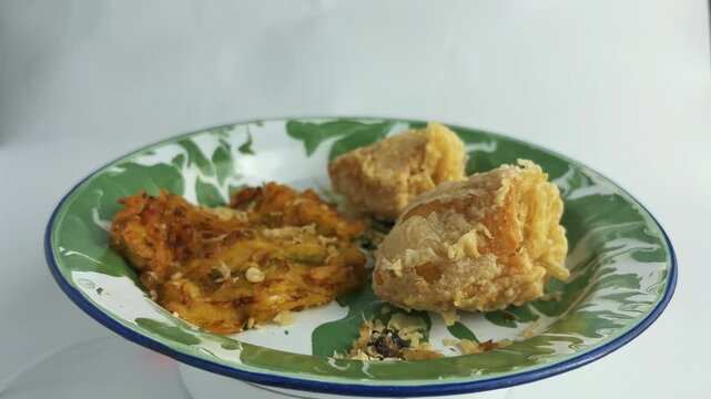 Indonesian fried snacks featuring bakwan and stuffed tofu on a green-white enamel plate. Traditional oily unhealthy street food. closeup. White background