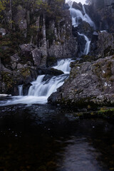 Obraz premium Waterfall tumbling over dark rocks into a still pool in Snowdonia