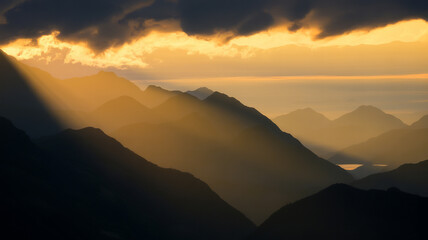 Sun rays shining through the clouds over mountain range at sunset