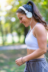 Woman walking outdoors in modern sports clothes and headphones, enjoying recreation and movement....