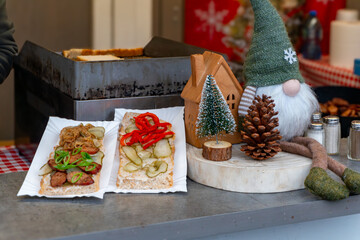 Sandwiches with pickles and vegetables at Christmas market, traditional street food flavors displayed among festive decorative stall elements and ornaments