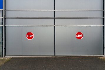 Two stop signs on industrial metal doors, symmetrical composition creating a minimalist urban scene focused on infrastructure and safety elements
