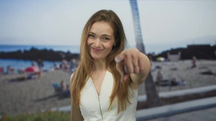 Woman smiling and pointing finger at camera under bright sunlight on sunny beach; attention confidence.