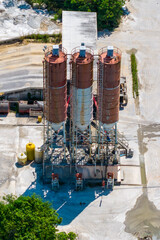 Aerial view of an industrial concrete batching plant with three prominent, tall material storage silos and surrounding machinery. © Jitti