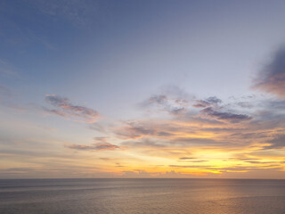 Wide aerial view of a pastel sunrise or sunset over a calm ocean, highlighting a single small boat beneath a softly colored cloudscape.