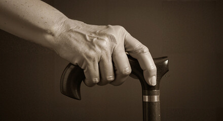 Elderly hand holding a wooden cane with a supportive grip  