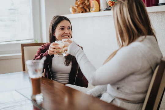 A cheerful indoor scene showing two women talking and sharing a moment with drinks, highlighting friendship and enjoyment in a relaxed atmosphere.