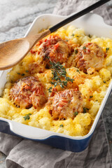 Casserole of meatballs and mashed potatoes with cheese, tomato sauce and herbs in a baking dish on the table. Vertical